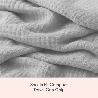 A close-up of soft, light gray, crinkled fabric with text below that reads: Newton Baby Compact Travel Crib Sheets fit compact travel cribs only.