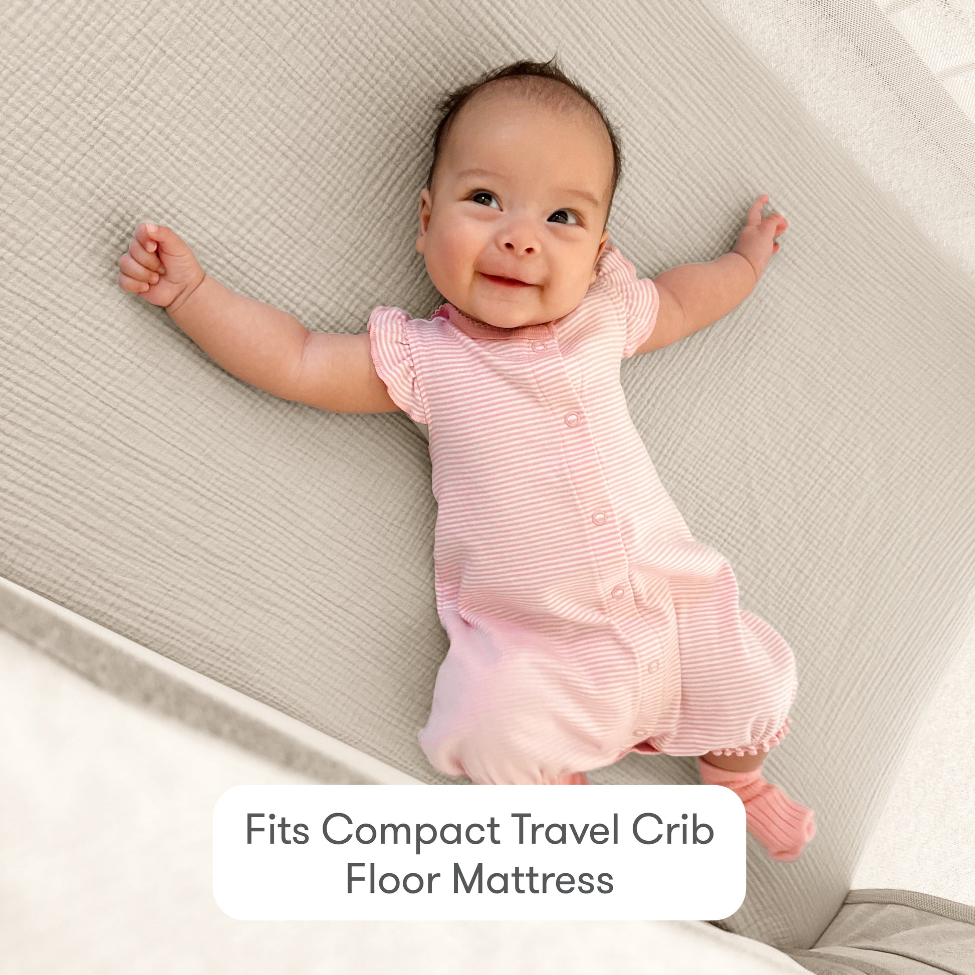 A smiling baby in a pink striped outfit lies on a light quilted mattress with Newton Baby Compact Travel Crib Sheets. Text below reads: Fits Compact Travel Crib Floor Mattress.