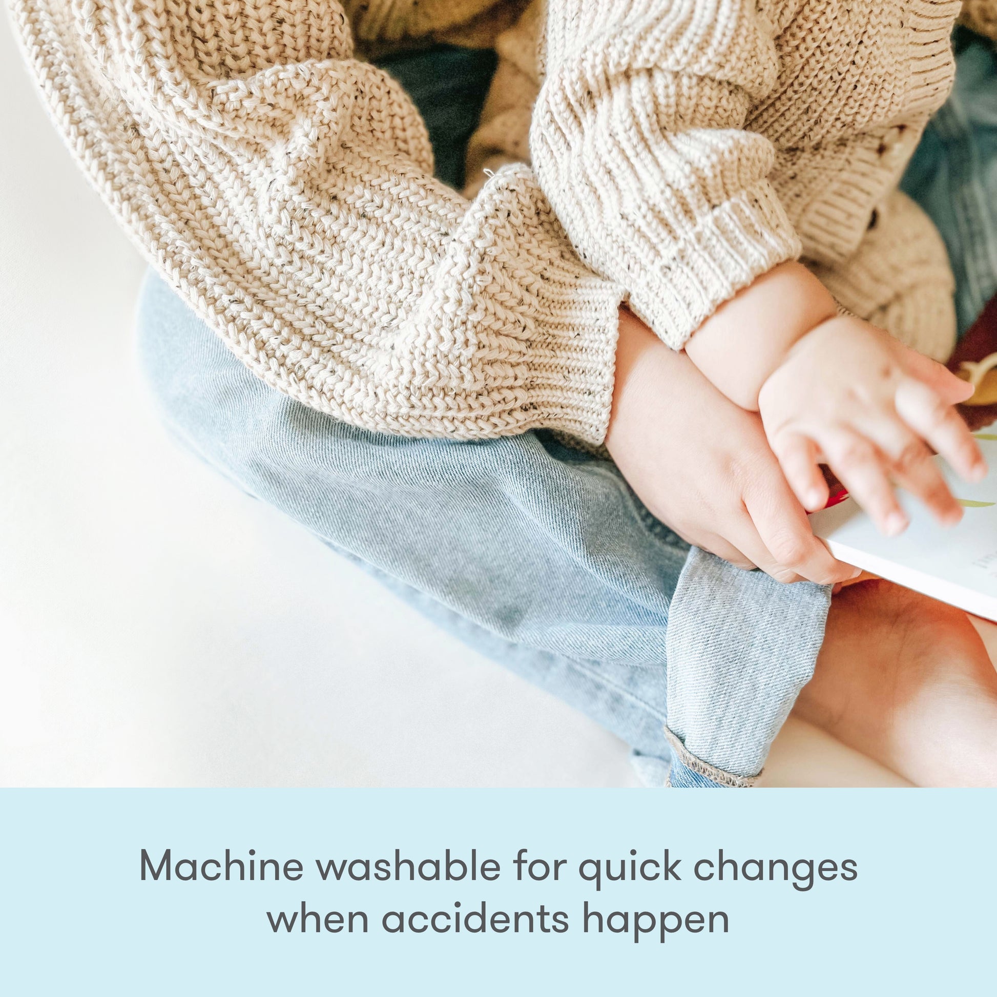 A child in a beige knit sweater and blue jeans sits on an adult’s lap, holding a book. Text below reads, “Newton Baby Waterproof Organic Twin Mattress Pad—machine washable for easy cleanups when accidents happen.”.