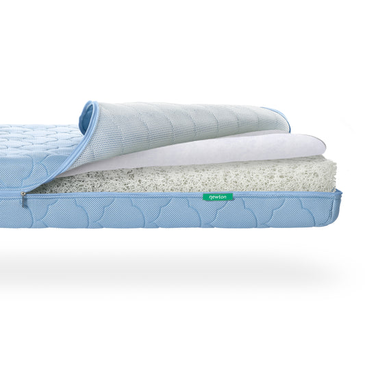 A Newton Baby Crib Mattress with the zippered cover partially peeled back to reveal a breathable, white, layered, webbed core. skip