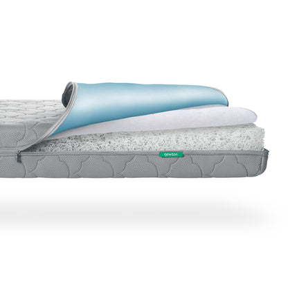 Cross-section of a Newton Baby Waterproof Crib Mattress showing a blue waterproof lining, a white foam-like layer, and a thick, porous inner core. 500-1001-GRY