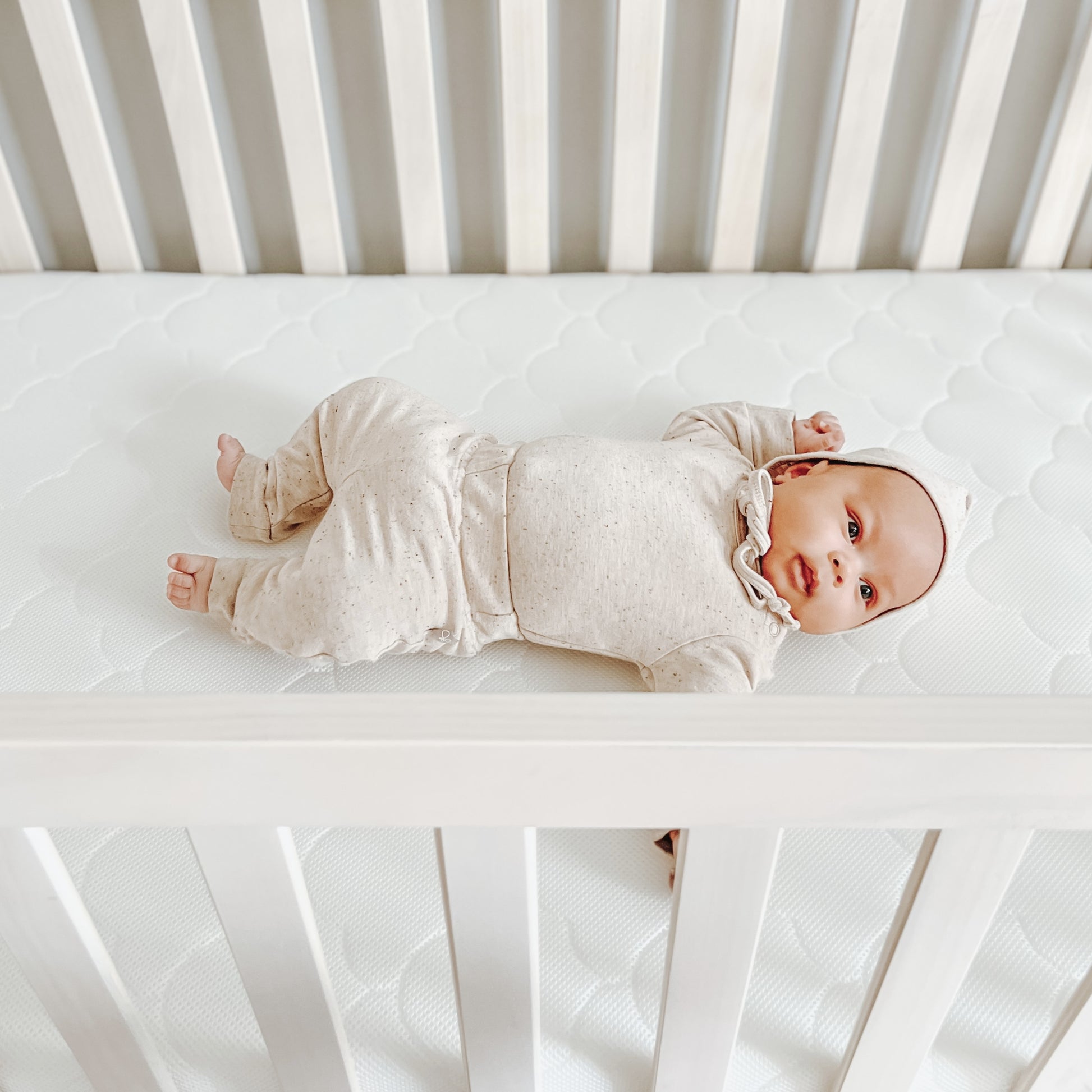 baby lying down on white newton waterproof mattress in crib in cute outfit.