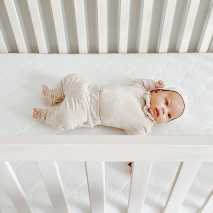 baby lying down on white newton waterproof mattress in crib in cute outfit.