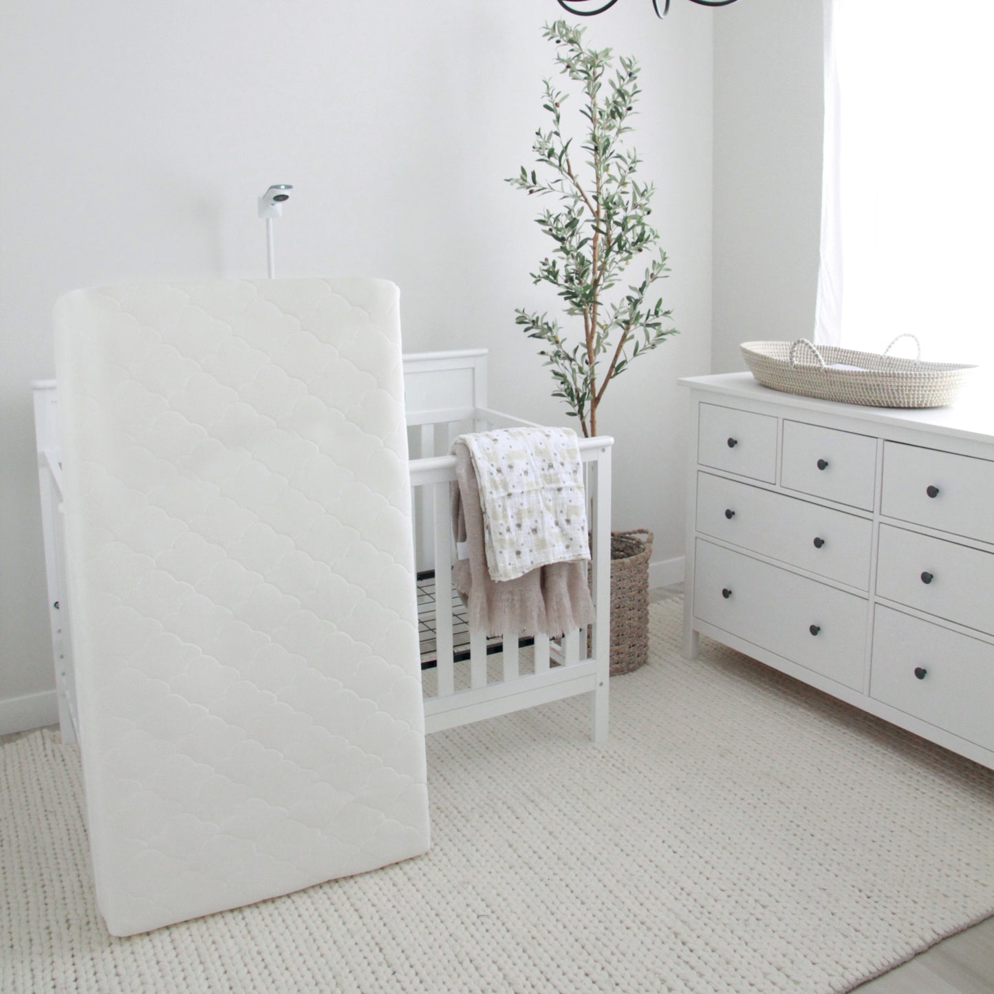 newton waterproof crib mattress leaning up against crib in all white nursery