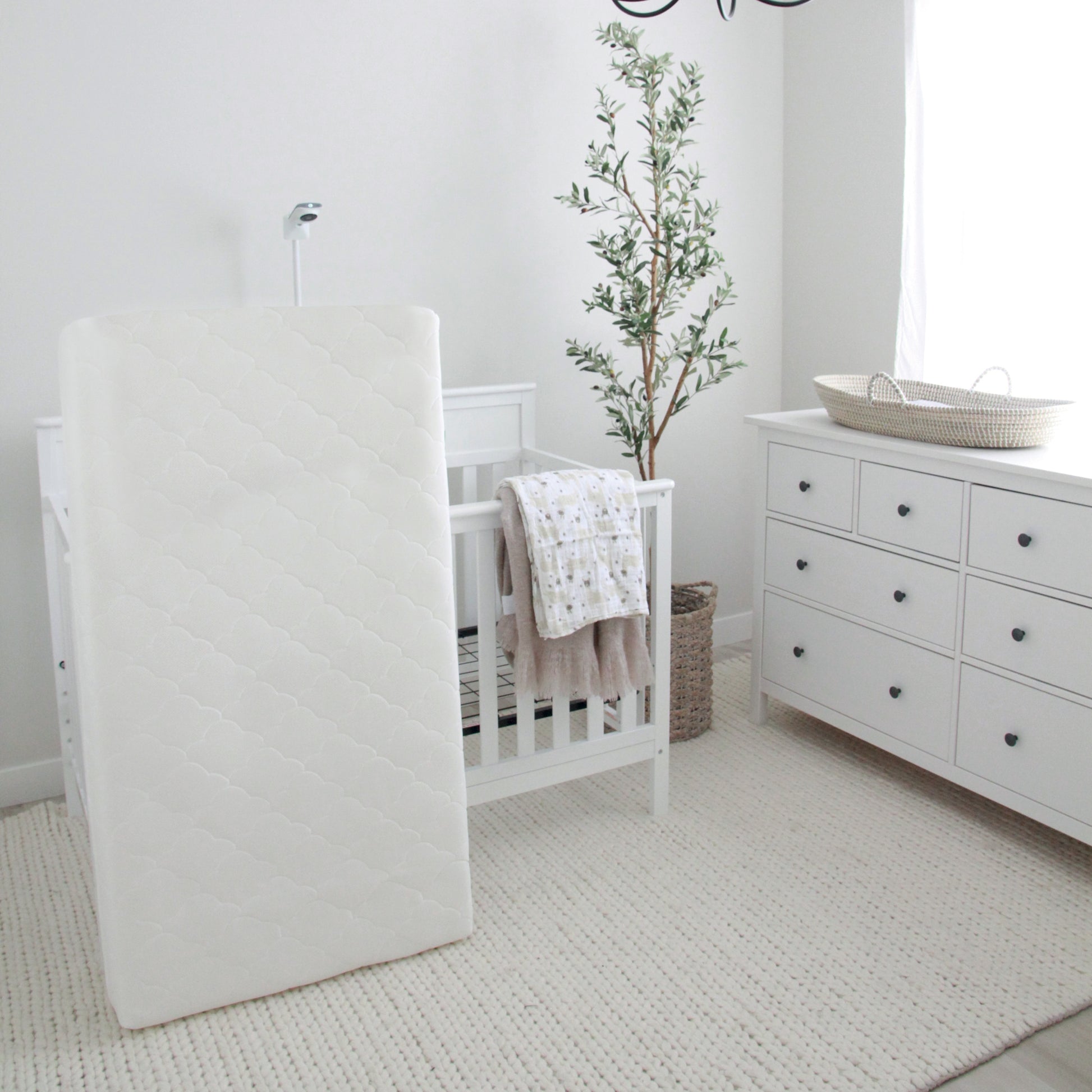 newton waterproof crib mattress leaning up against crib in all white nursery