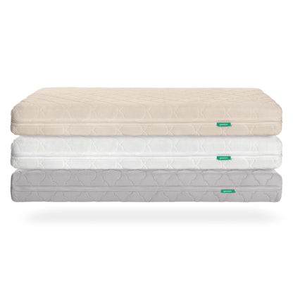Three stacked Newton Baby Waterproof Crib Mattresses in beige, white, and light gray display a subtle geometric pattern and a green label. Each breathable mattress includes a washable cover, shown against a white background.