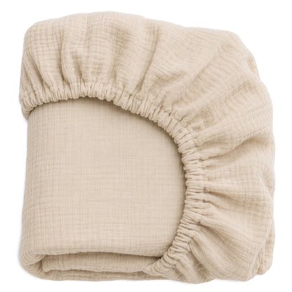 A beige, textured Newton Baby Nest Bassinet Extra Sheet—breathable and neatly folded—displays its elastic edge and gathered fabric at one corner.