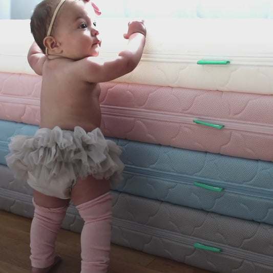 Video of baby standing next to stacked mattresses, smiling baby standing and laying in crib, dad breathing through mattress then washing mattress.