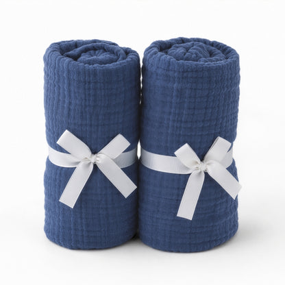 Two rolled, dark blue towels, tied with white bows and standing upright side by side on a white background, resemble Newton Baby's Breathable, Organic Cotton Sheets (2-pack).