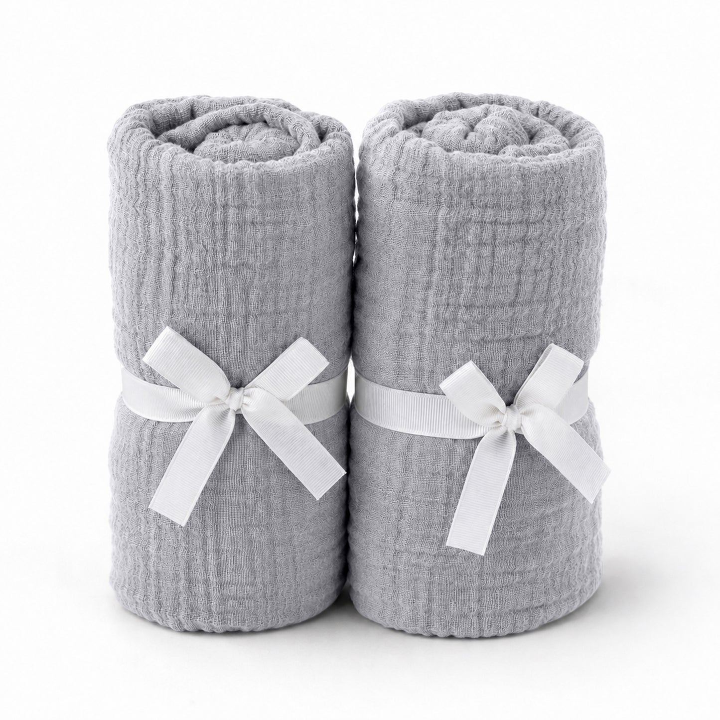 Two light gray towels, rolled and tied with white ribbons, stand side by side—an elegant pairing for Newton Baby's Breathable, Organic Cotton Sheets (2-pack), perfect for adding comfort and style to any serene nursery.
