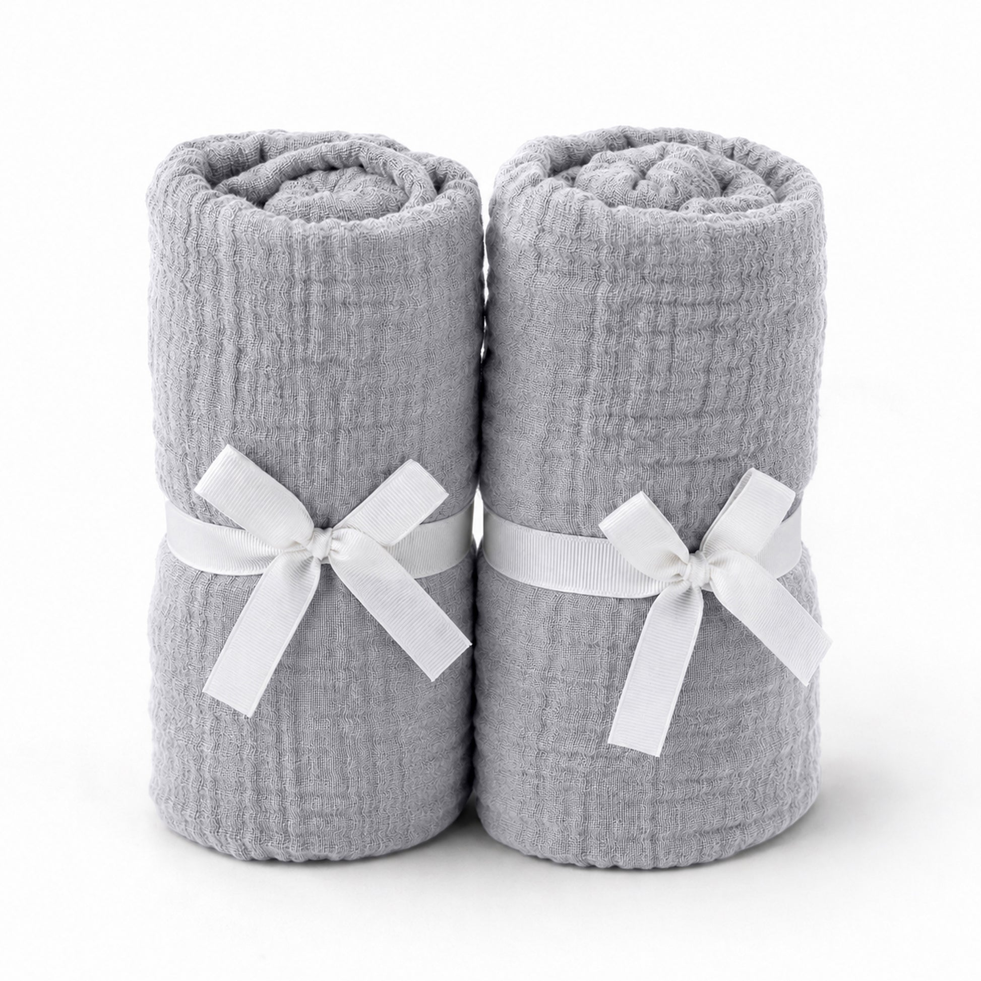 Two light gray towels, rolled and tied with white ribbons, stand side by side—an elegant pairing for Newton Baby's Breathable, Organic Cotton Sheets (2-pack), perfect for adding comfort and style to any serene nursery.