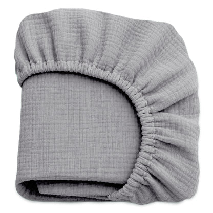 A folded, light gray Newton Baby Breathable, Organic Cotton Sheet (2-pack), made from crinkled muslin with elastic edges, is shown against a white background. 999-3020-EVG