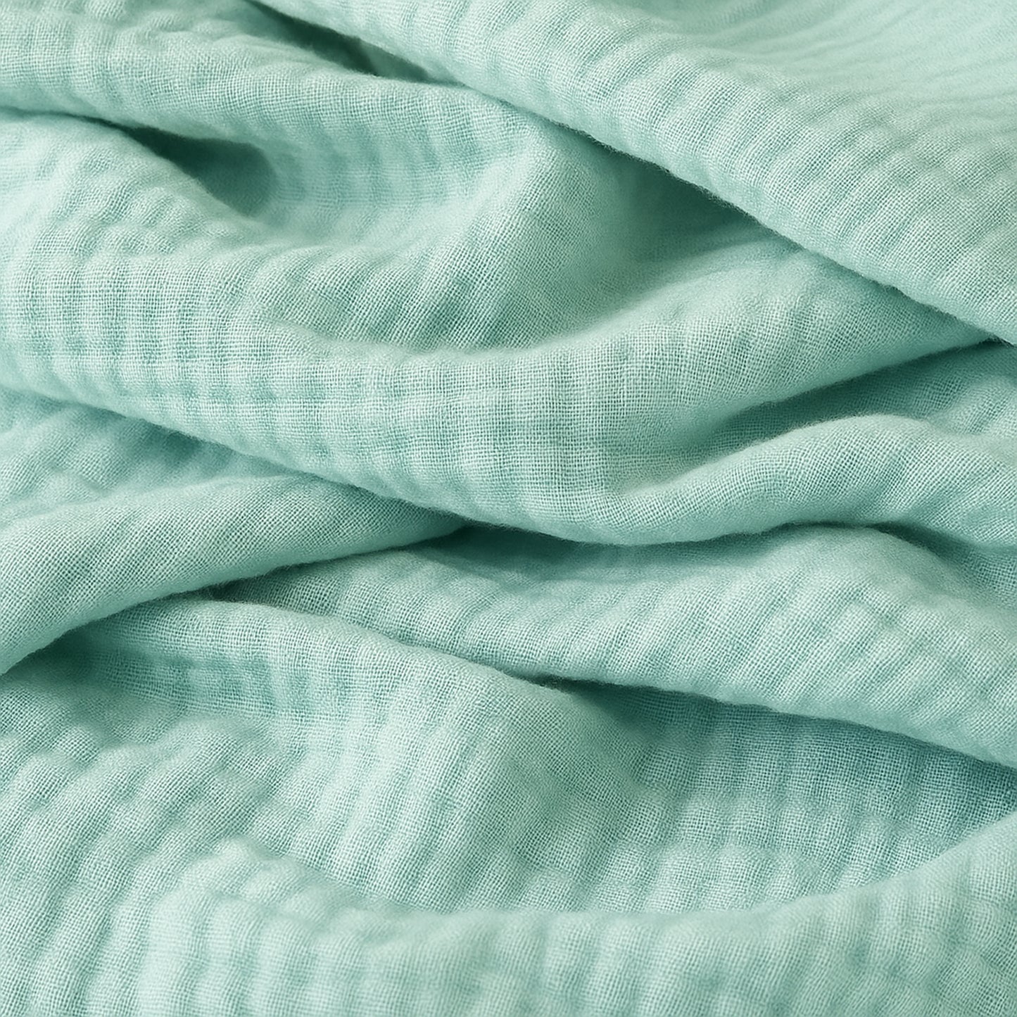 A close-up of Newton Baby Breathable, Organic Cotton Sheets (2-pack) in soft light green, featuring a crinkled texture, gentle folds, and a subtle grid-like pattern.