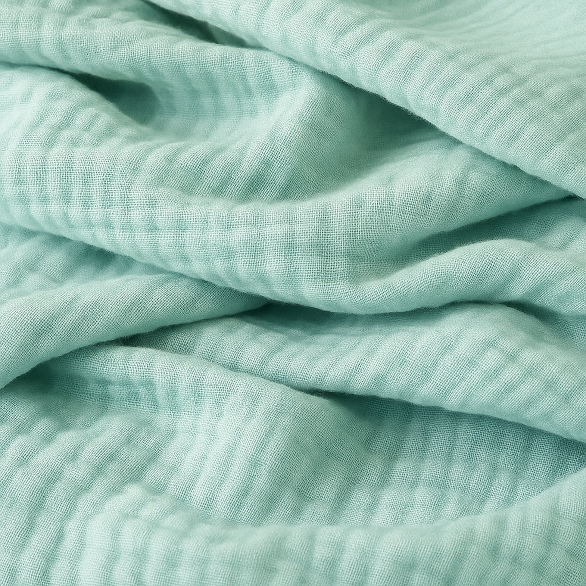 A close-up of Newton Baby Breathable, Organic Cotton Sheets (2-pack) in soft light green, featuring a crinkled texture, gentle folds, and a subtle grid-like pattern.