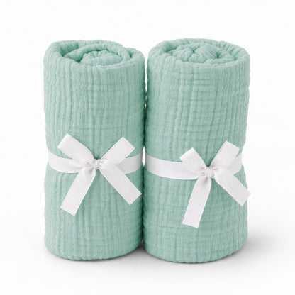 Two rolled, mint green Newton Baby Breathable, Organic Cotton Sheets (2-pack) stand upright side by side, each tied with a white ribbon around the middle, shown on a plain white background.