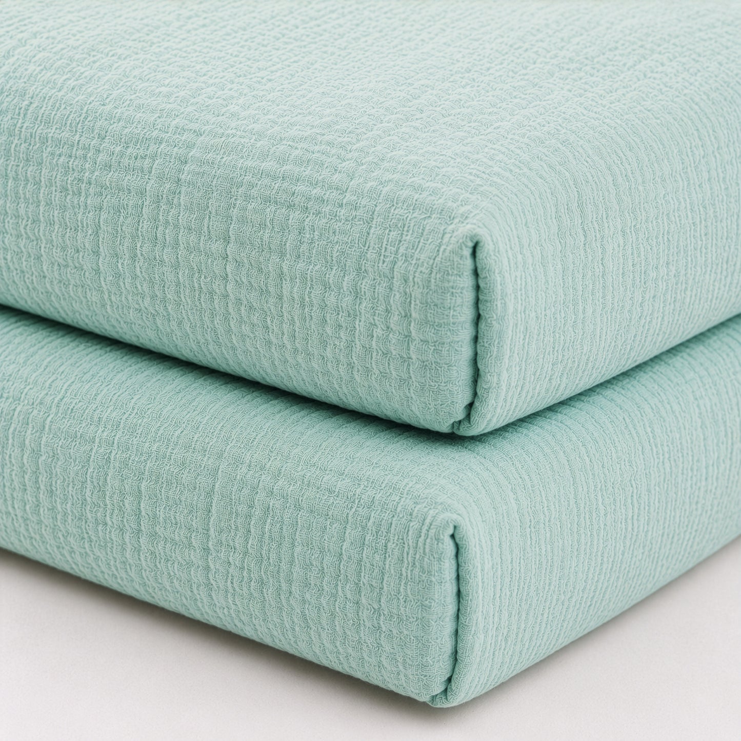 Two neatly stacked, folded Newton Baby Breathable, Organic Cotton Sheets (2-pack) are displayed on a white surface. Made from soft cotton with a subtle grid pattern, these sheets offer a cozy, inviting look and feel.