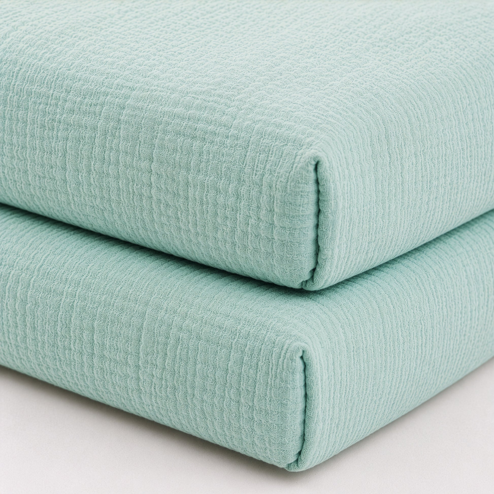 Two neatly stacked, folded Newton Baby Breathable, Organic Cotton Sheets (2-pack) are displayed on a white surface. Made from soft cotton with a subtle grid pattern, these sheets offer a cozy, inviting look and feel.