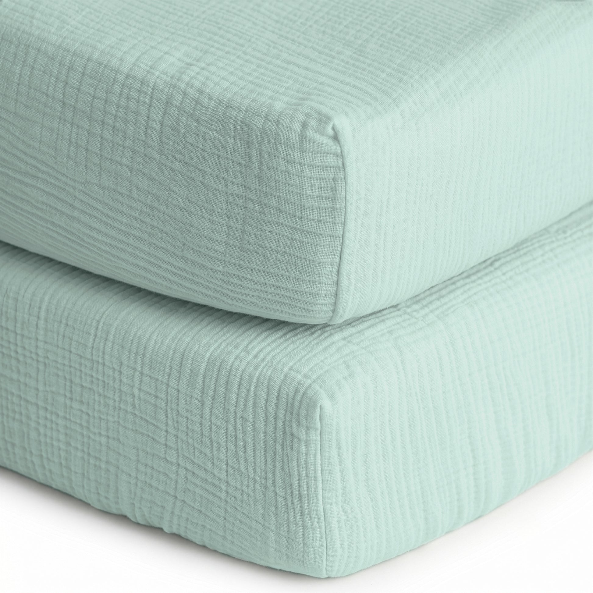 Two stacked, light blue, textured sheets from Newton Baby—a 2-pack of breathable, organic cotton sheets—feature a soft quilted pattern, resembling cozy baby bedding.