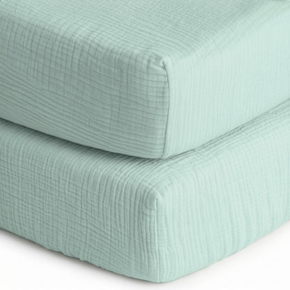 Two stacked, light blue, textured sheets from Newton Baby—a 2-pack of breathable, organic cotton sheets—feature a soft quilted pattern, resembling cozy baby bedding.