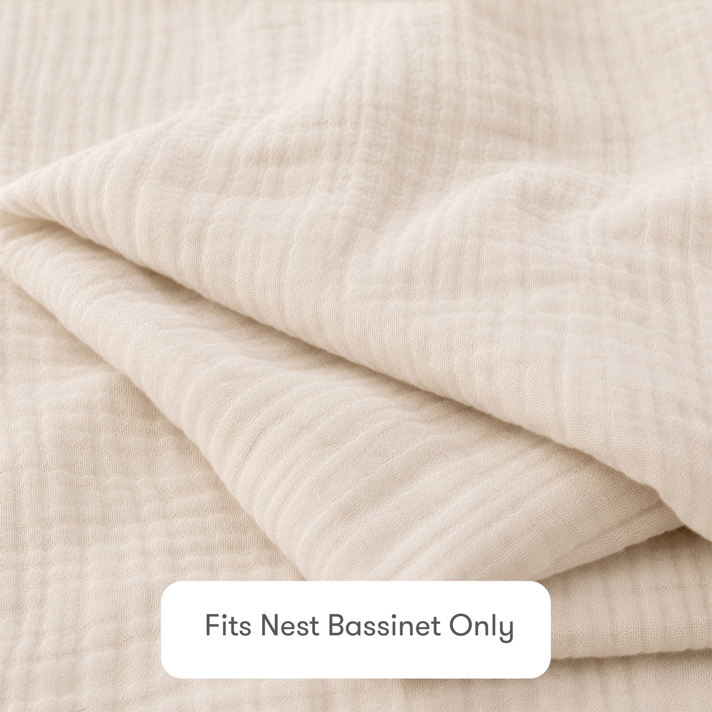 A close-up of a folded, cream-colored Newton Baby Nest Bassinet Extra Sheet made from textured cotton muslin. A label reads “Fits Nest Bassinet Only”—ideal for those wanting breathable sheets for their baby's crib.