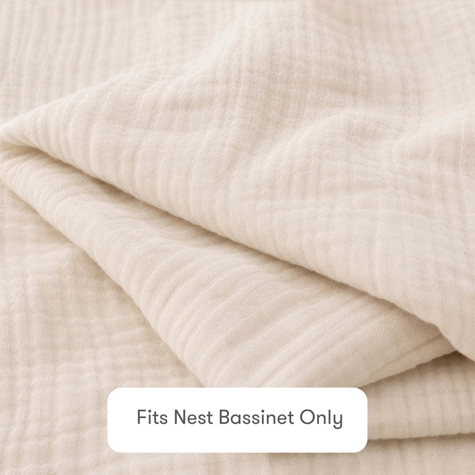 A close-up of a folded, cream-colored Newton Baby Nest Bassinet Extra Sheet made from textured cotton muslin. A label reads “Fits Nest Bassinet Only”—ideal for those wanting breathable sheets for their baby's crib.