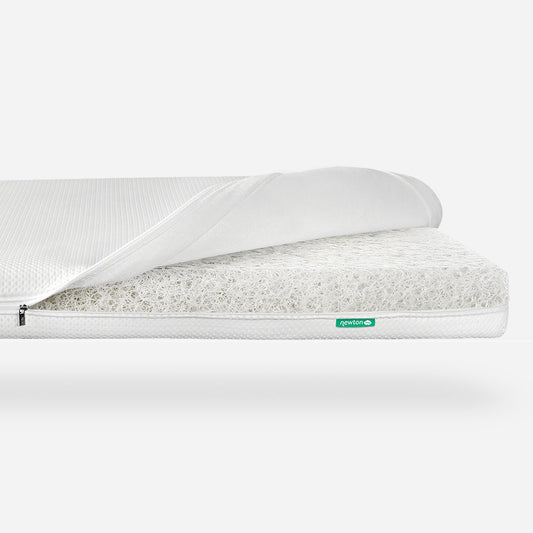Crib mattress with a breathable design, partially shown with its cover peeled back, displaying its inner core structure, tagged with a small 'Newton' logo.