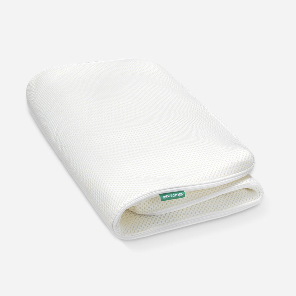 A rolled-up Newton baby mattress cover showing its breathable design, with the Newton logo visible on the edge.