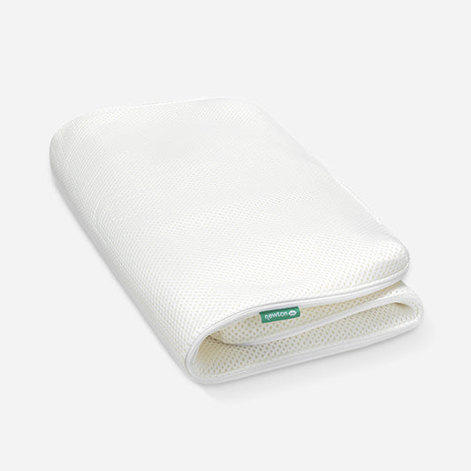 White breathable Newton baby mattress cover folded over on one corner, displaying a green label with the logo 'Newton'. skip