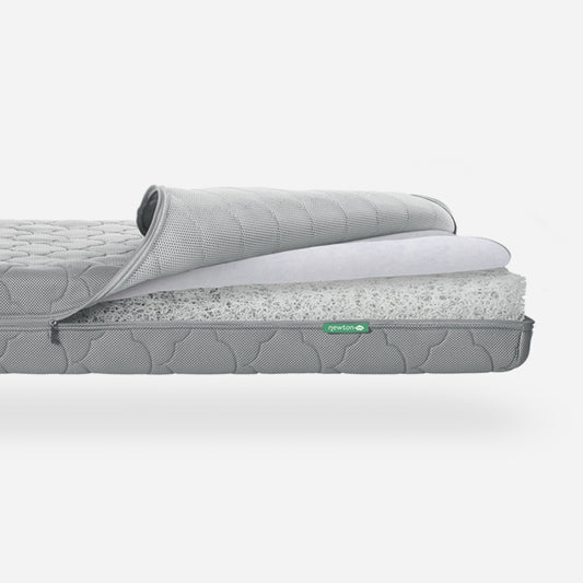 Newton Baby Crib Mattress partially unrolled to show its breathable design and washable materials, featuring a small Newton logo. skip