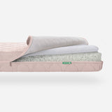Newton Baby crib mattress with pink cover with a visible cross-section to show breathable layers and a stitched Newton logo. skip