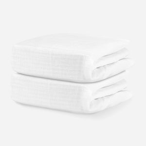 Two neatly stacked white cotton baby blankets on a solid white background. skip