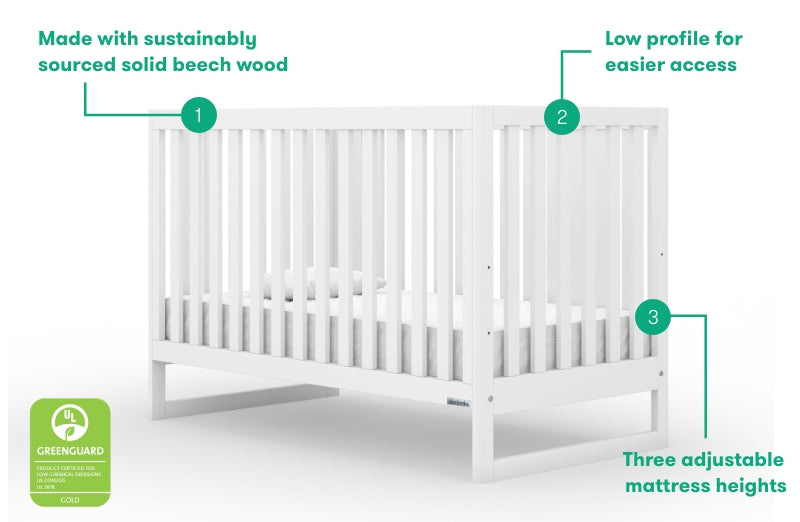 White solid beech wood crib with low profile for easier access, featuring three adjustable mattress heights and a GREENGUARD Gold certification label.