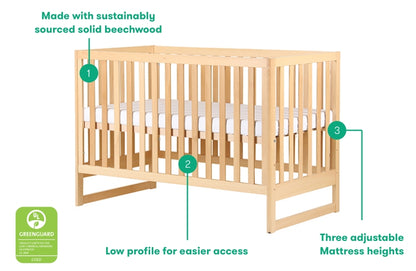 A sustainable solid beechwood crib featuring a low profile for easier access and three adjustable mattress heights, marked with labels "1", "2", and "3"; text includes "Made with sustainably sourced solid beechwood", "Low profile for easier access", and "Three adjustable Mattress heights". Additionally, there’s a green "Greenguard" certification logo on the left.