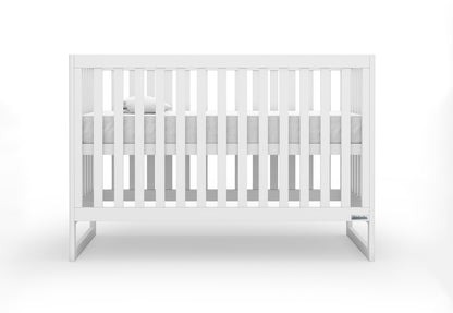 A minimalist white baby crib with slender bars and a visible Newton Baby logo on one end.