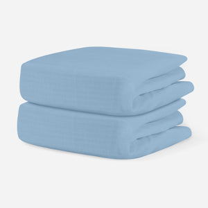 Stack of two sky blue crib sheets on a white background. skip