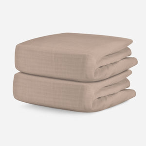 Stack of two neatly folded tan crib sheets on a white background. skip