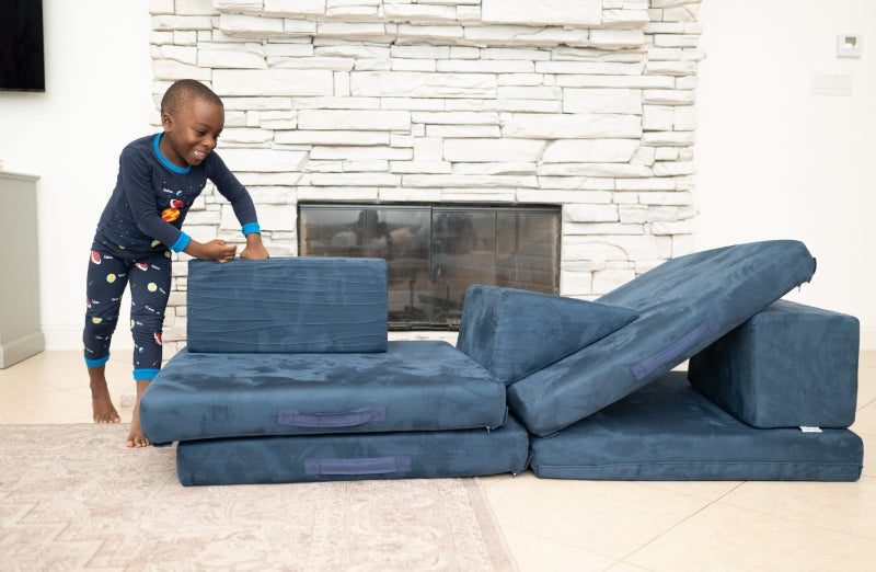 A young child in pajamas plays with large modular foam blocks in a living room.