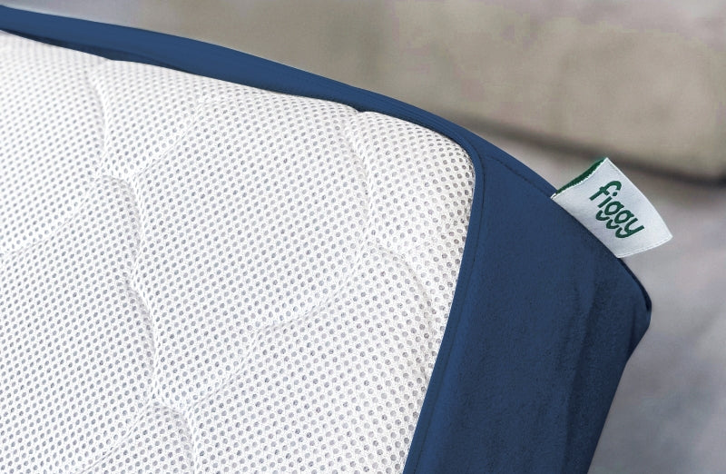 Close-up view of a breathable crib mattress with a white perforated surface and navy blue trim, featuring a 'figgy' label.