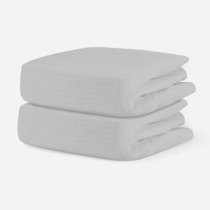 Two folded pale gray breathable crib sheets on a white background. skip