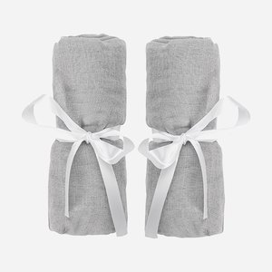 Two rolled-up light gray Travel Crib & Play Yard Sheets, each tied with a white satin ribbon, are placed side by side on a plain white background.