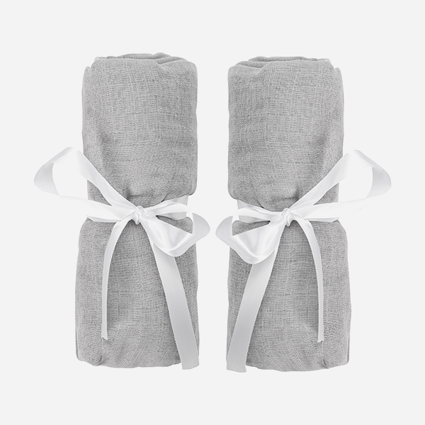 Two rolled-up light gray Travel Crib & Play Yard Sheets, each tied with a white satin ribbon, are placed side by side on a plain white background.