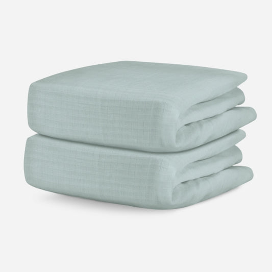 Two folded pale green, breathable baby crib sheets displayed on a neutral background. skip