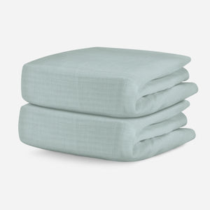 Two folded pale green, breathable baby crib sheets displayed on a neutral background. skip