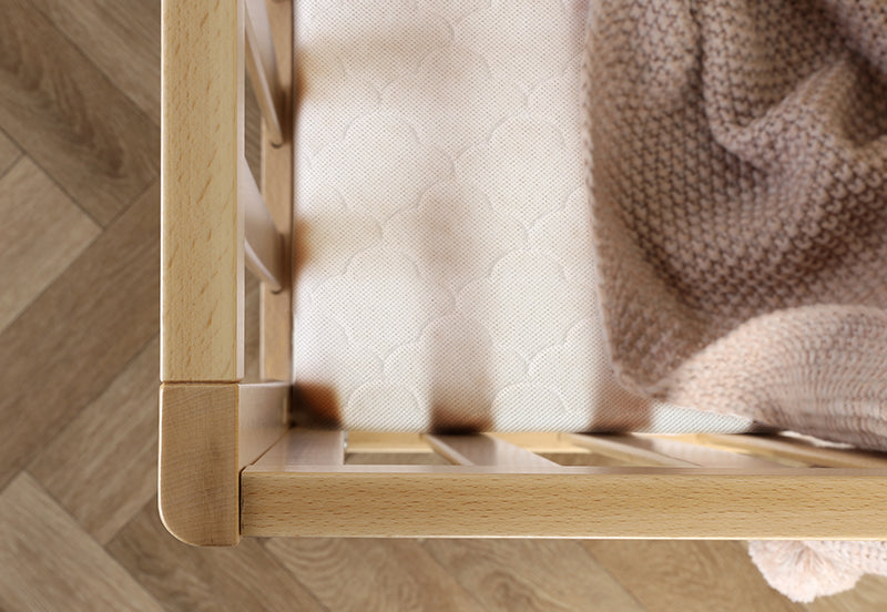 Close-up of a light wood crib with a breathable crib mattress adorned with a geometric pattern, and a soft tan knit blanket draped over the side.