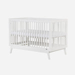 The dadada baby Soho Convertible Crib is a white wooden 3-in-1 crib with slatted sides, mid-century style, and four angled legs. It comes with a white Newton crib mattress for comfort.