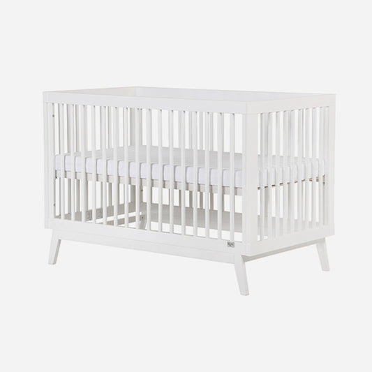 The dadada baby Soho Convertible Crib is a white wooden 3-in-1 crib with slatted sides, mid-century style, and four angled legs. It comes with a white Newton crib mattress for comfort.